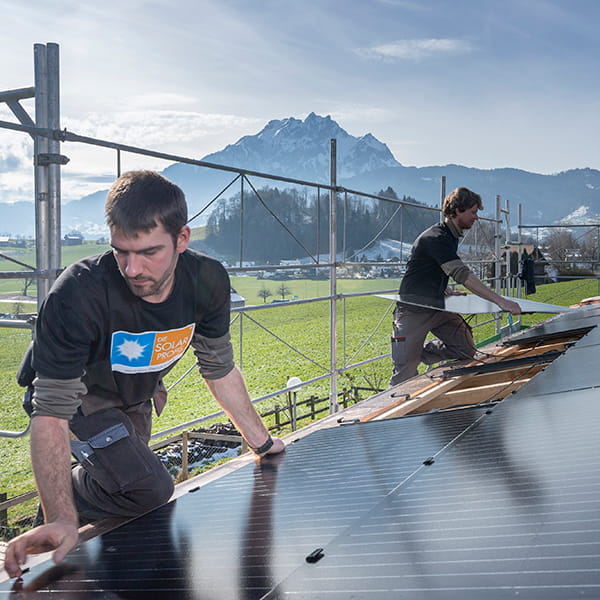 Zwei Männer montieren eine Indach-Solaranlage vor einem Bergpanorama